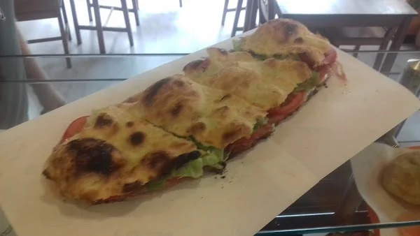 Una focaccia lunga farcita con pomodoro, insalata e formaggio filante, appena tagliata sul banco.