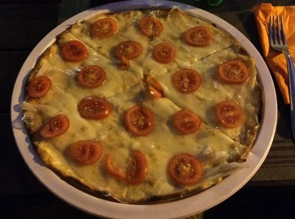 Una pizza tonda coperta di formaggio fuso e fette di pomodorino, già divisa in spicchi nel piatto.